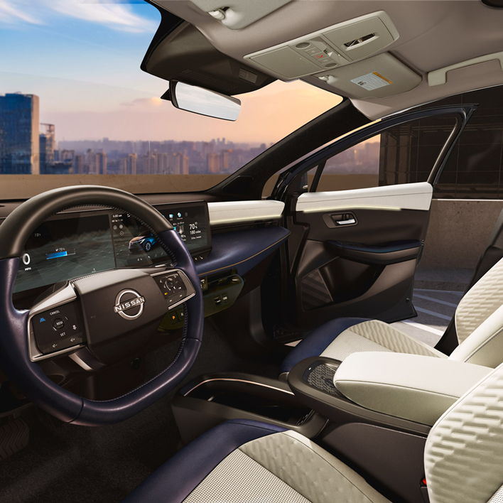 Interior of a Nissan car with beige and dark blue seating, dashboard, and steering wheel, city skyline view.